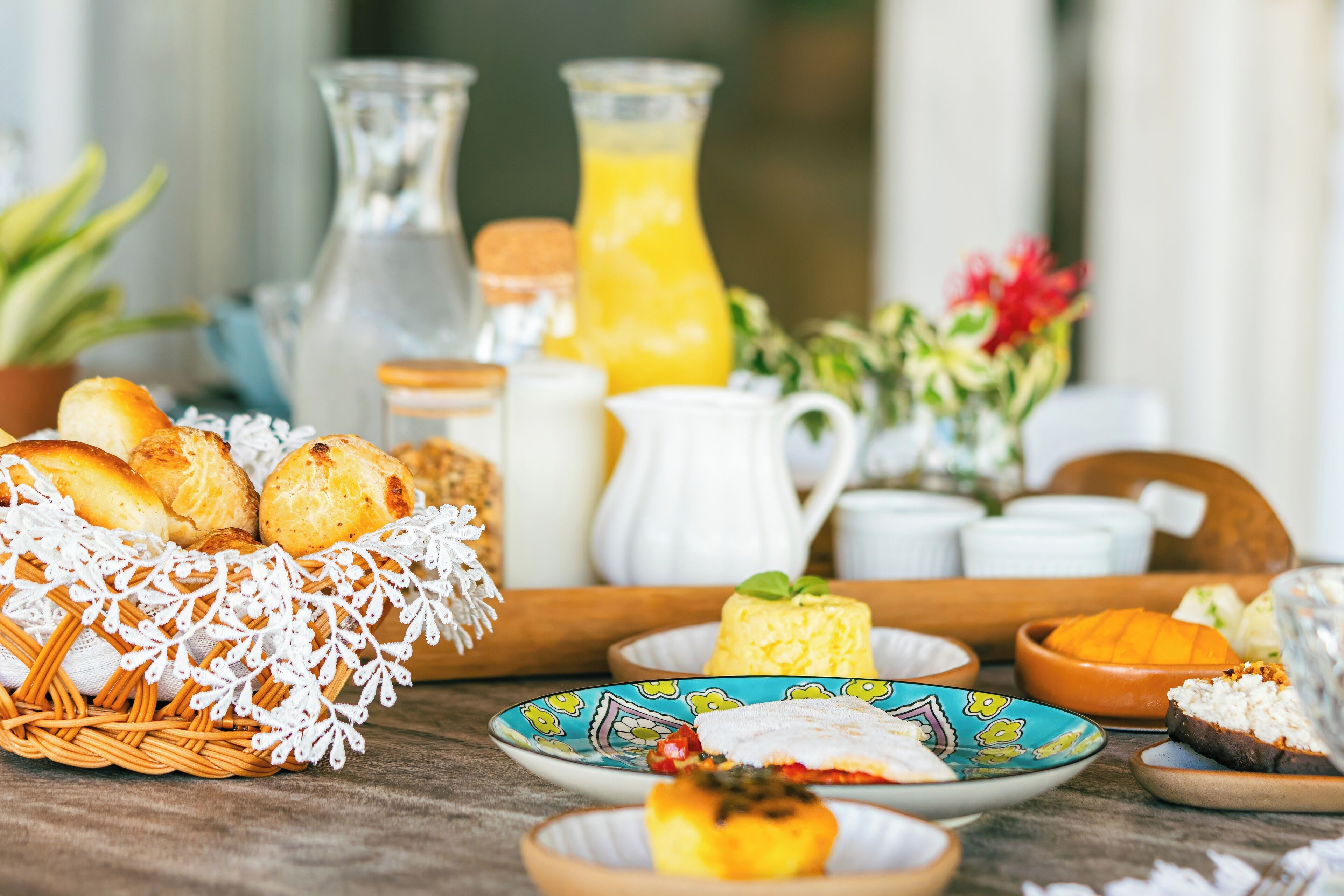 A breakfast setting with bread, pastries, and a fruit bowl on a wooden table.