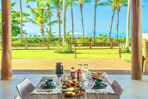 A dining table set with breakfast items, a view of the ocean, and palm trees. - Casa Mandala Corumbau (Corumbau)