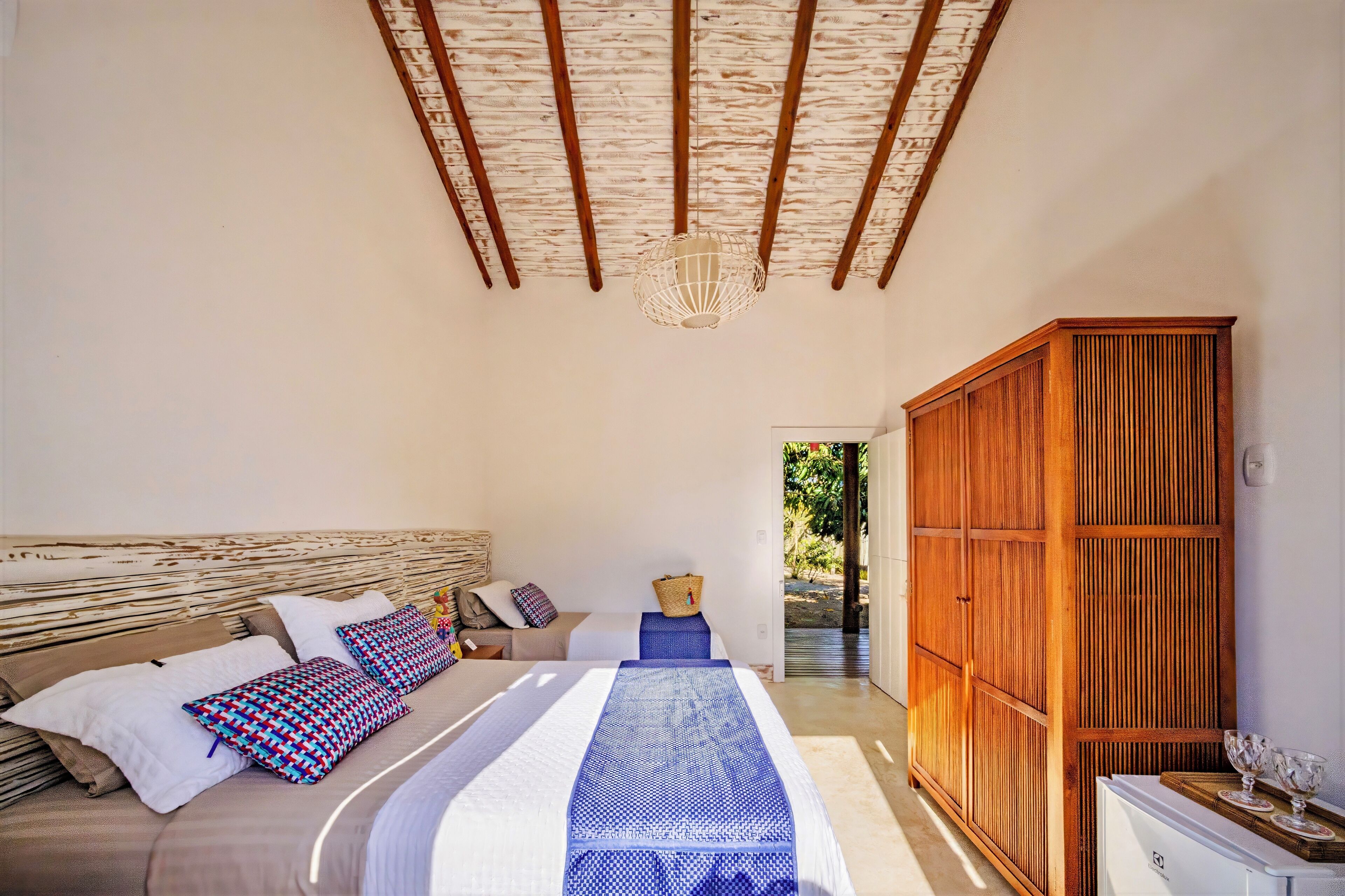 A bedroom with a bed, a wooden wardrobe, and a view of the outdoors.