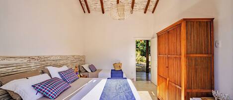 A bedroom with a bed, a wooden wardrobe, and a view of the outdoors.