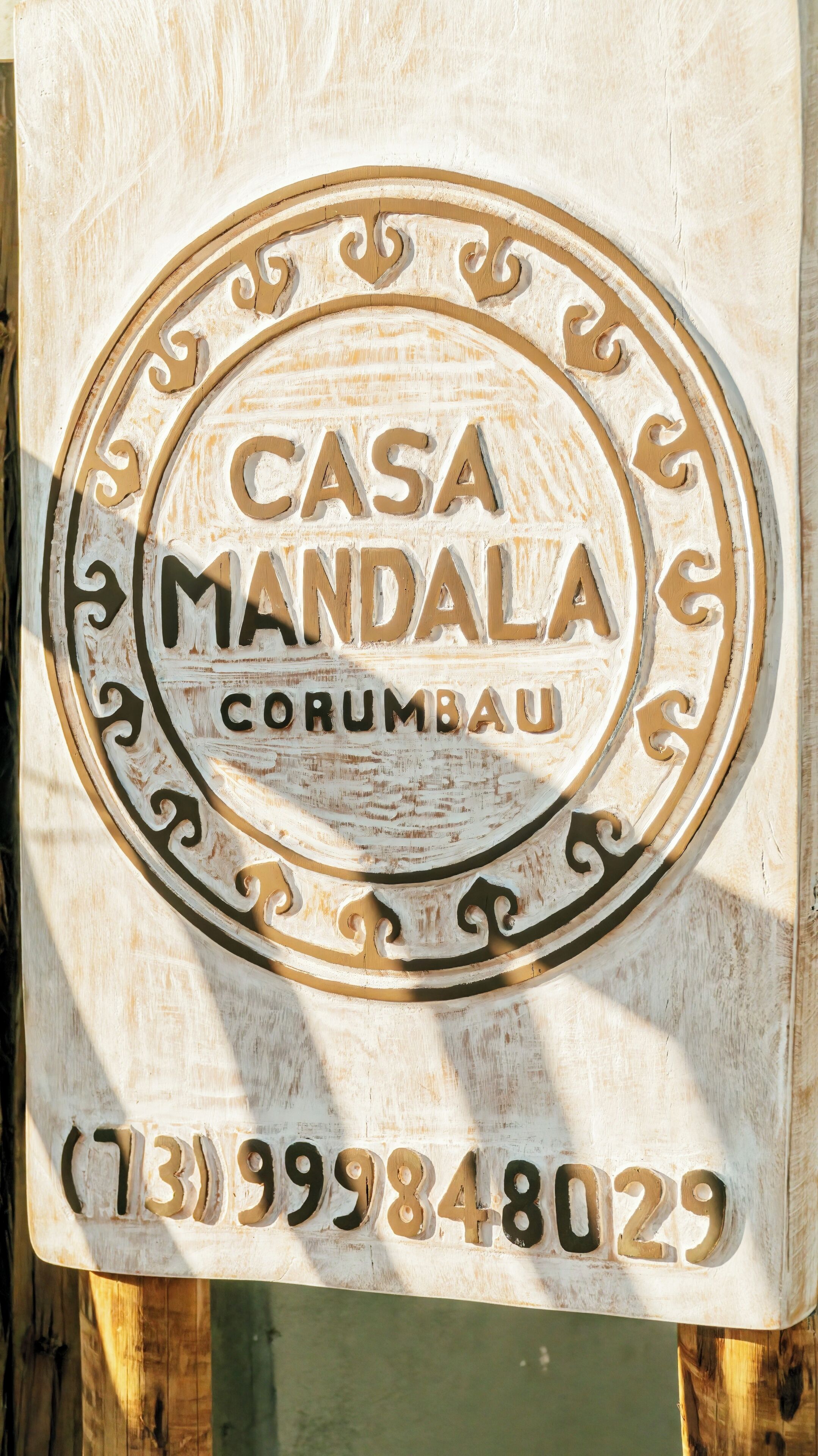 Un panneau en bois portant l’inscription « CASA MANDALA CORUMBAU » et un numéro de téléphone.