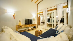 A bedroom with a bed, a TV, a wooden side table, and a wicker ottoman. - Casa Mandala Corumbau (Corumbau)
