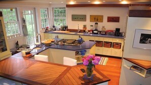 Een moderne keuken met een centraal eiland, houten vloeren en uitzicht op de omgeving door grote ramen.