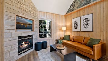 Un salon chaleureux avec une cheminée en pierre, des murs en bois, un canapé en cuir et des œuvres d’art encadrées.