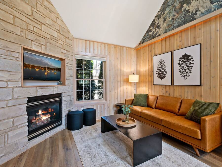 Un salon chaleureux avec une cheminée en pierre, des murs en bois, un canapé en cuir et des œuvres d’art encadrées.