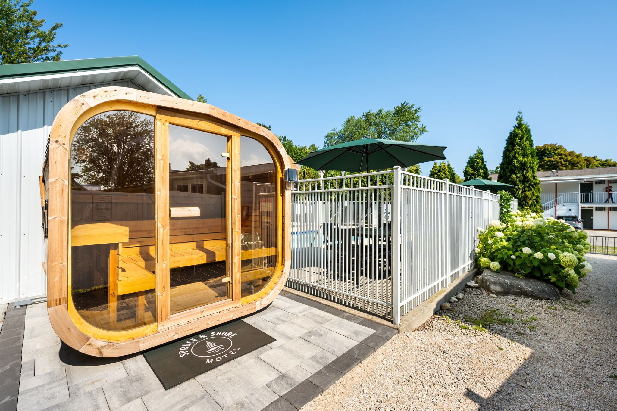 A wooden structure with glass doors, a white fence, and a sign for 'Spruce & Shore Motel'.