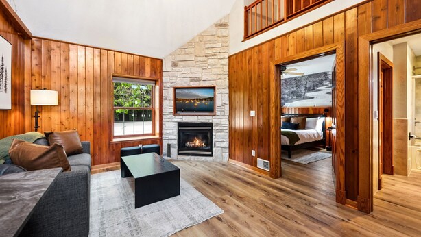 A cozy living room with a stone fireplace, wooden walls, and a comfortable seating area.