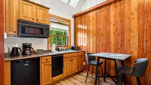 A kitchen with wooden cabinets, a microwave, a coffee maker, and a dishwasher. There is a window with a view of greenery outside.