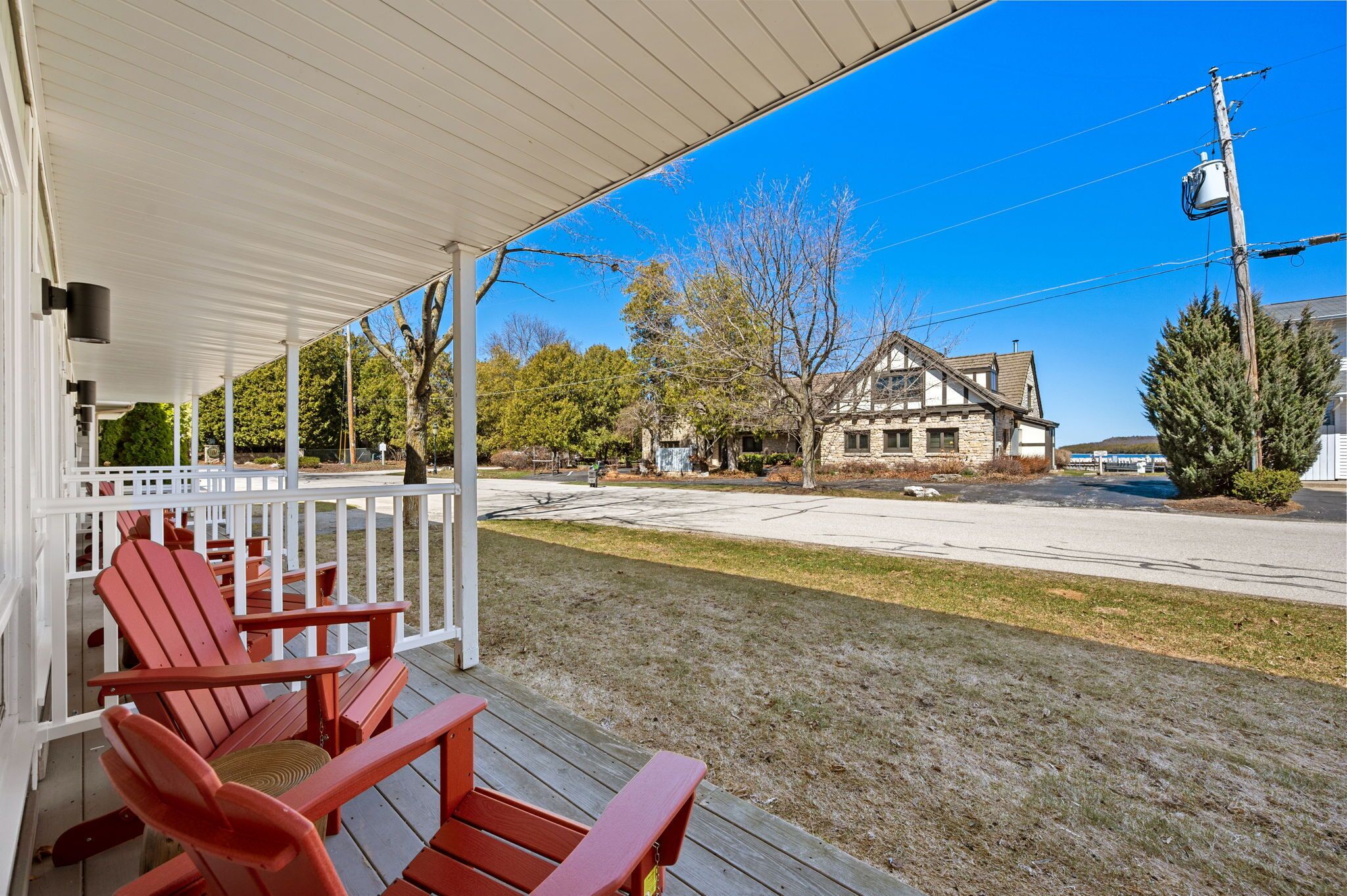 A covered porch with red Adirondack chairs, a stone building in the background, and a clear blue sky.