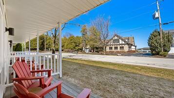 A covered porch with red Adirondack chairs, a stone building in the background, and a clear blue sky.