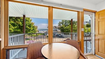 A room with a large sliding glass door leading to a balcony with a view of a marina and boats. There is a round table with two chairs in the room.