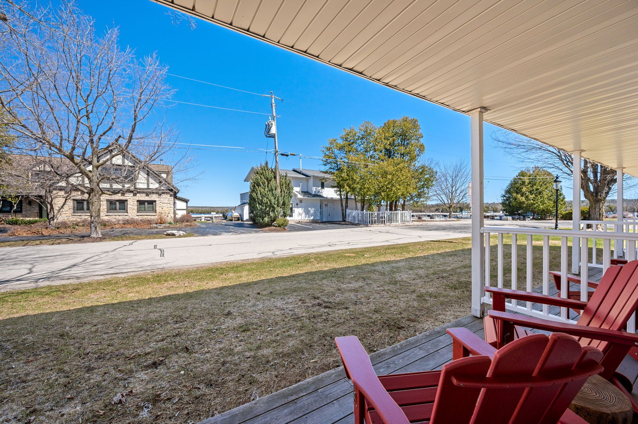 A covered porch with red Adirondack chairs, a view of a street, and a building with a stone facade.