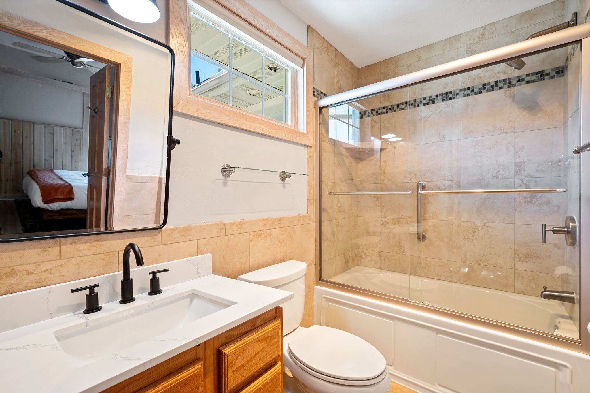 A modern bathroom with a large mirror, a sink with black faucets, a toilet, and a glass-enclosed shower area.