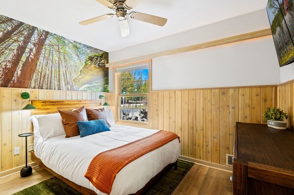 A bedroom with a bed, a window, a ceiling fan, and a wooden wall paneling.