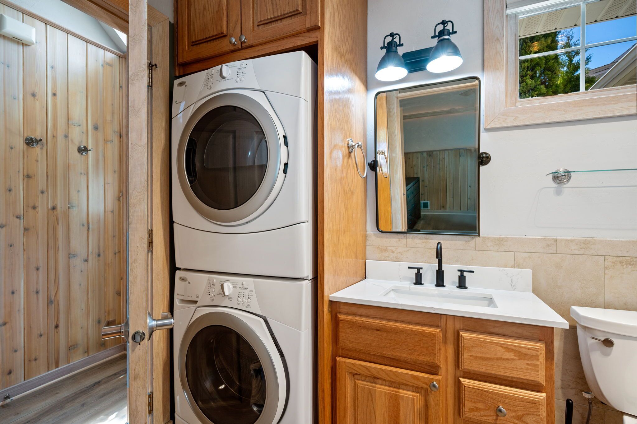 A laundry room with two stacked washing machines, a sink, and wooden cabinets.