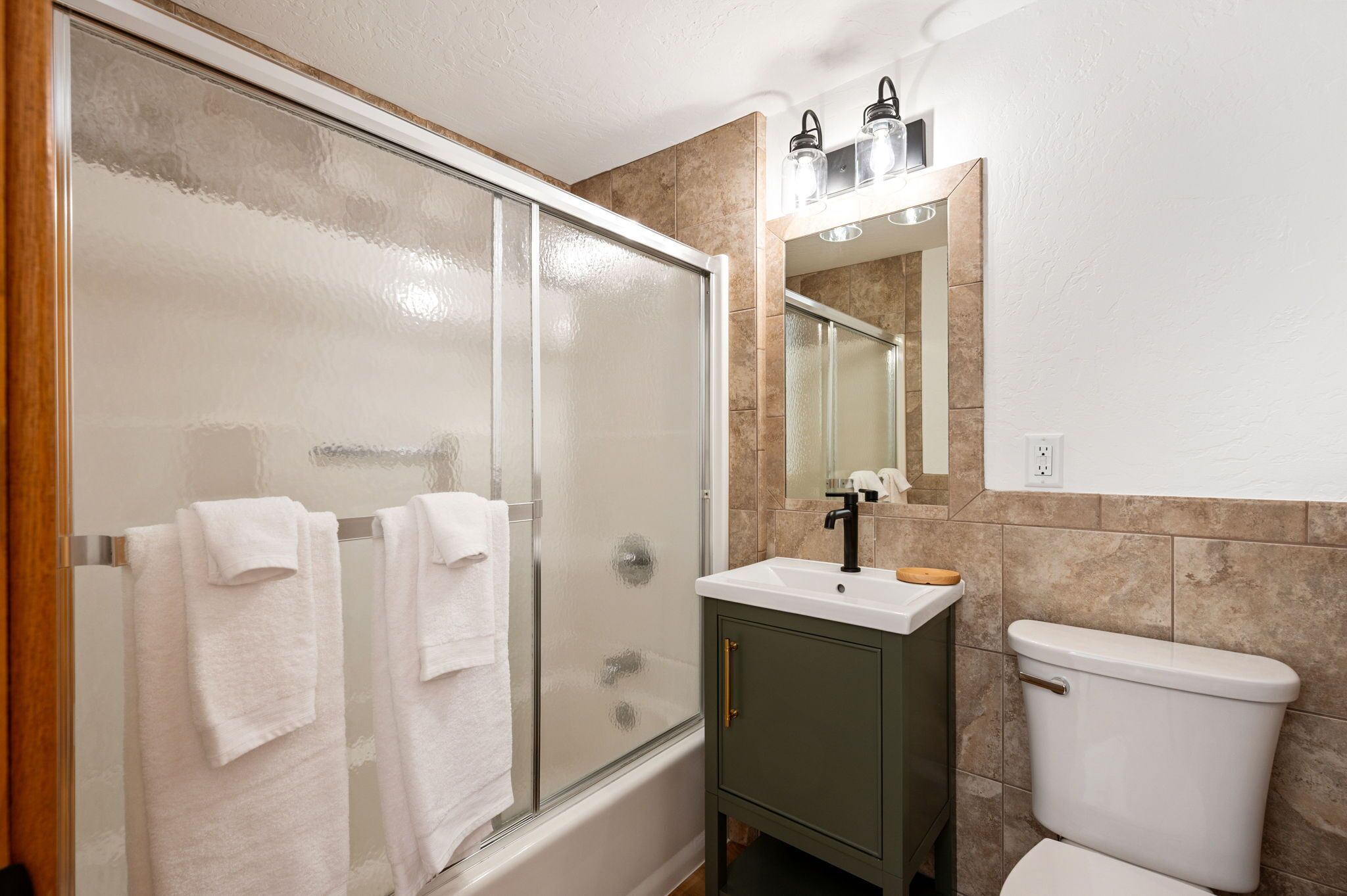 A bathroom with a glass shower enclosure, a white sink, a mirror, and a toilet.
