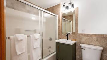 A bathroom with a glass shower enclosure, a white sink, a mirror, and a toilet.