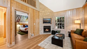 A cozy living room with a stone fireplace, wooden walls, and a comfortable seating area.
