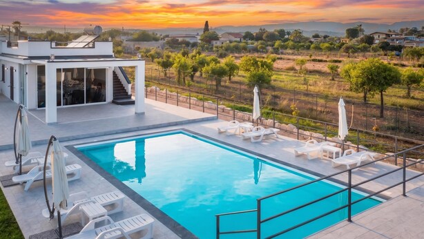 A swimming pool with lounge chairs and umbrellas, a modern building with a glass facade, and a scenic sunset view. - Villa Dei Tre Colli - Noto (Noto)