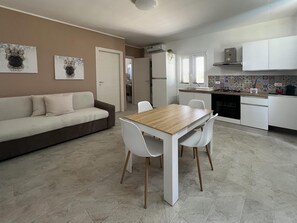 Un soggiorno moderno con un divano, un tavolo da pranzo con sedie, un angolo cottura con mobili e un fornello, e opere d'arte appese al muro.