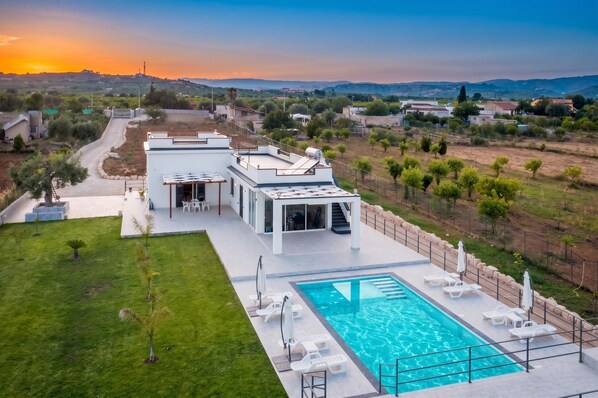 Eine moderne Villa mit Swimmingpool, Sitzgelegenheiten im Freien und Blick auf die umliegende Landschaft.
