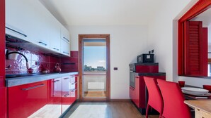 A compact kitchen with red cabinets, a wooden door, and a view through the door.