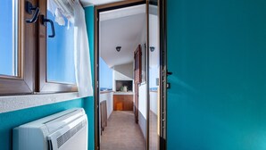A narrow hallway with a view of a kitchen and a balcony.