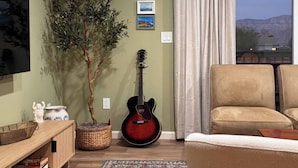 Un salon avec une guitare, une plante en pot, un canapé et un téléviseur.