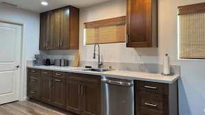 Une cuisine moderne avec des meubles en bois, un lave-vaisselle en acier inoxydable et une fenêtre équipée de stores.