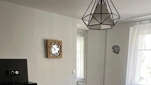 Una cocina compacta con lavavajillas, una mesa de madera con cuatro sillas, una lámpara colgante y un reloj de pared.