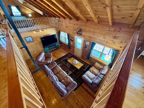 A spacious cabin with a loft bedroom, a living area with leather sofas, a TV, and a fireplace.