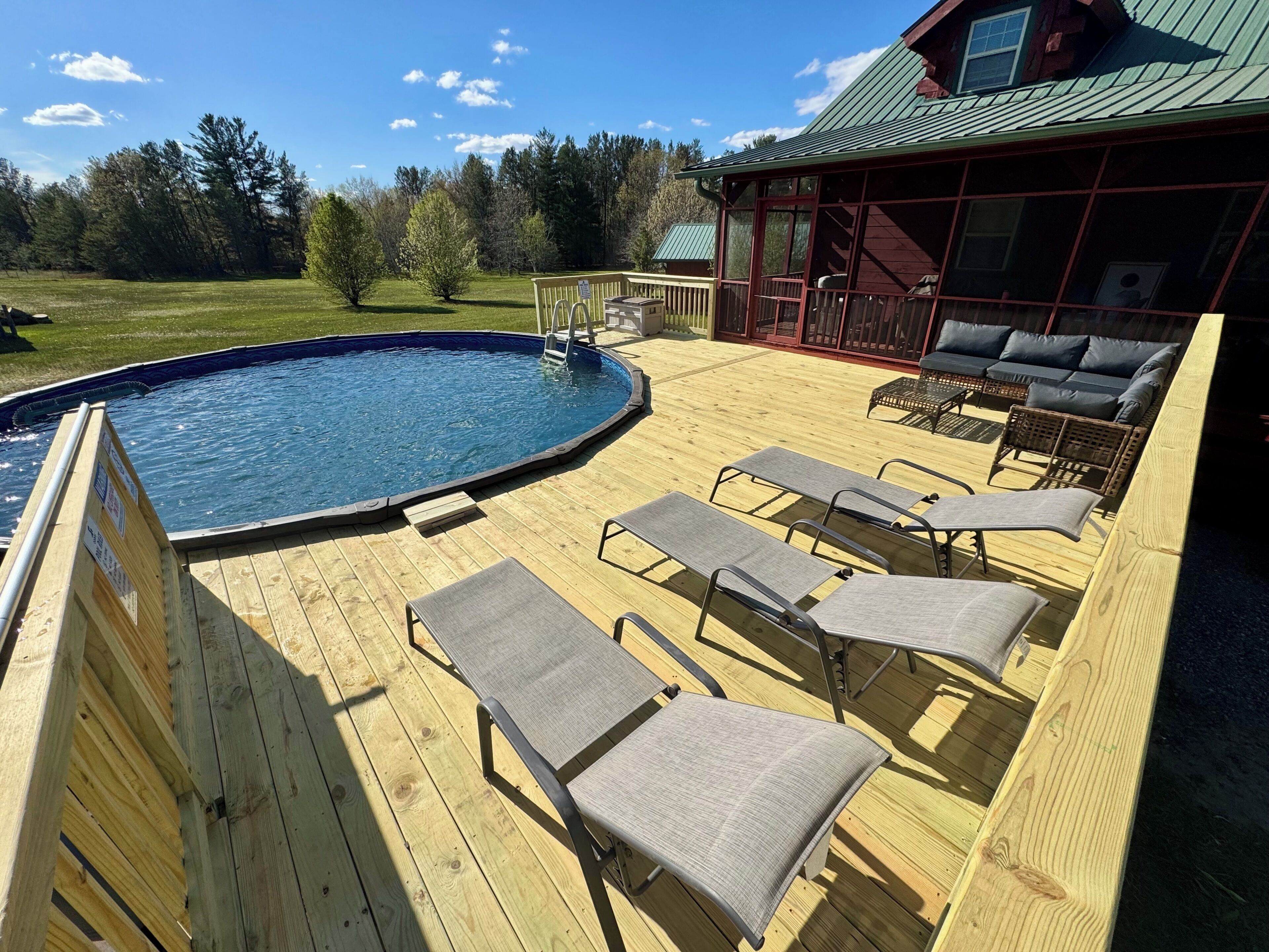 Eine Holzterrasse mit Pool, Liegestühlen und einem überdachten Sitzbereich.