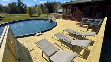 Eine Holzterrasse mit Pool, Liegestühlen und einem überdachten Sitzbereich.