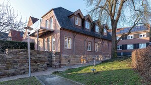 Une maison à deux étages, construite en briques, avec un toit en pente, un mur en pierre et un chemin menant à l’entrée.
