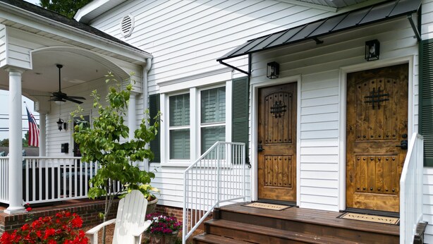 A white house with a wooden front door, a porch with a white chair, and a red flower pot. - Beautiful,comfortable, safe suite with private entrance. (Dallas)