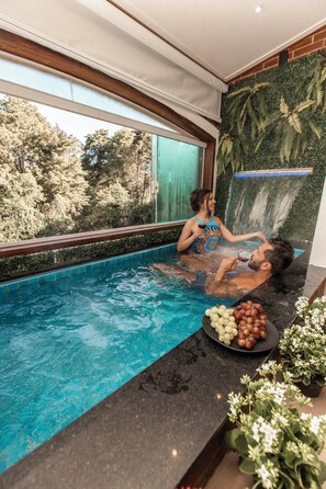A private hot tub area with a waterfall backdrop, a pool, and a table with grapes.