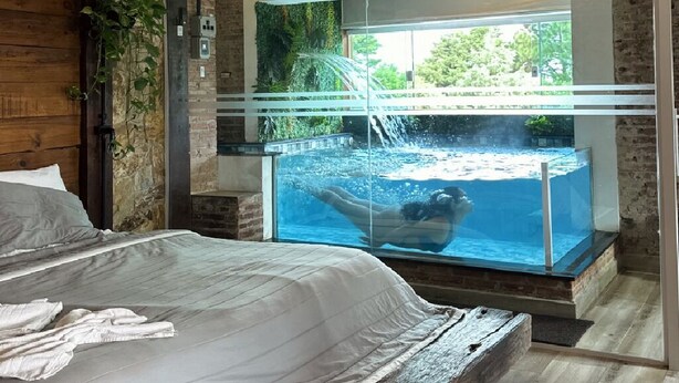 A bedroom with a large window overlooking a swimming pool. - Roteiros Adorai (Piedade)