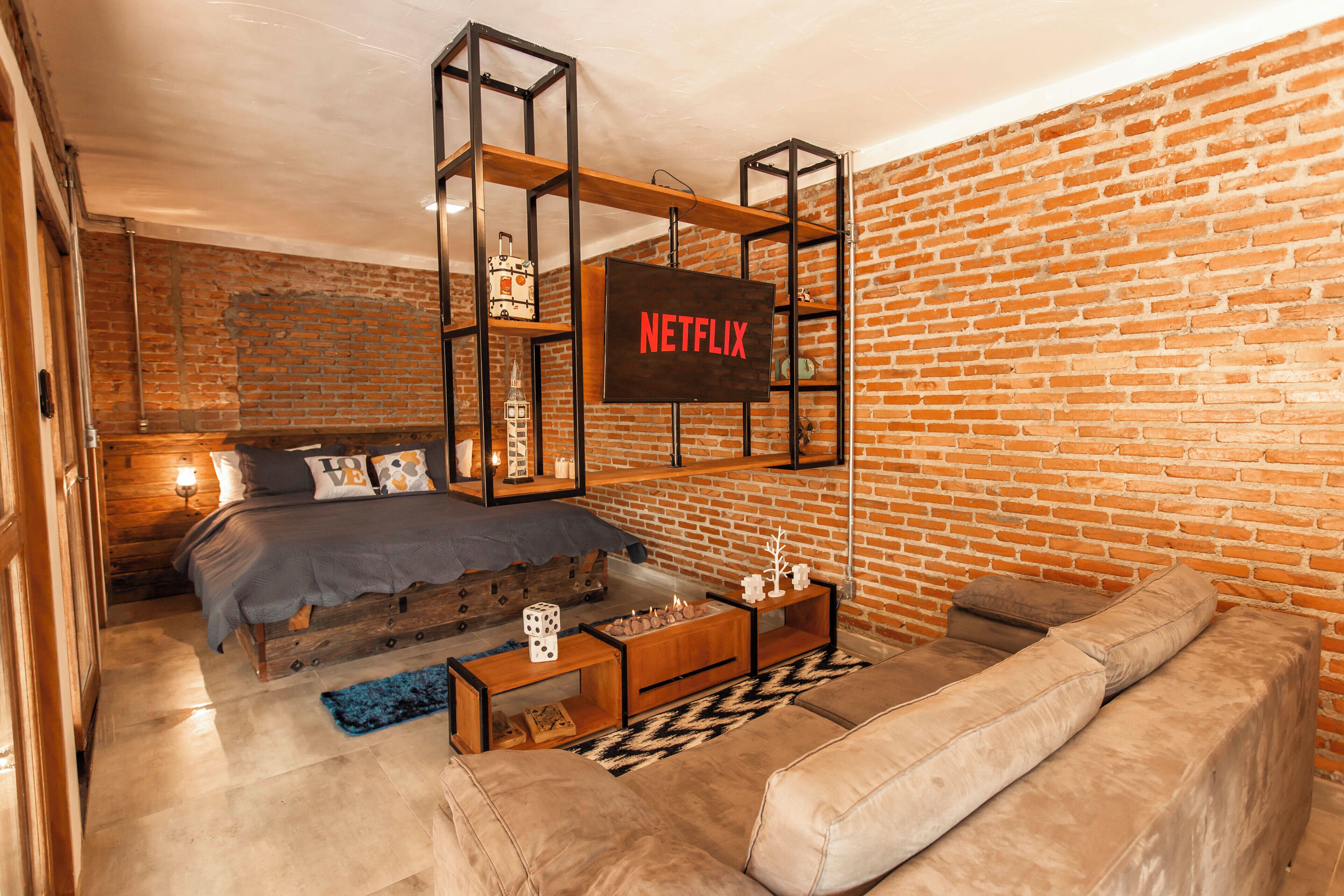 A cozy room with a brick wall, a bed with a blue blanket, a wooden coffee table, and a leather sofa.