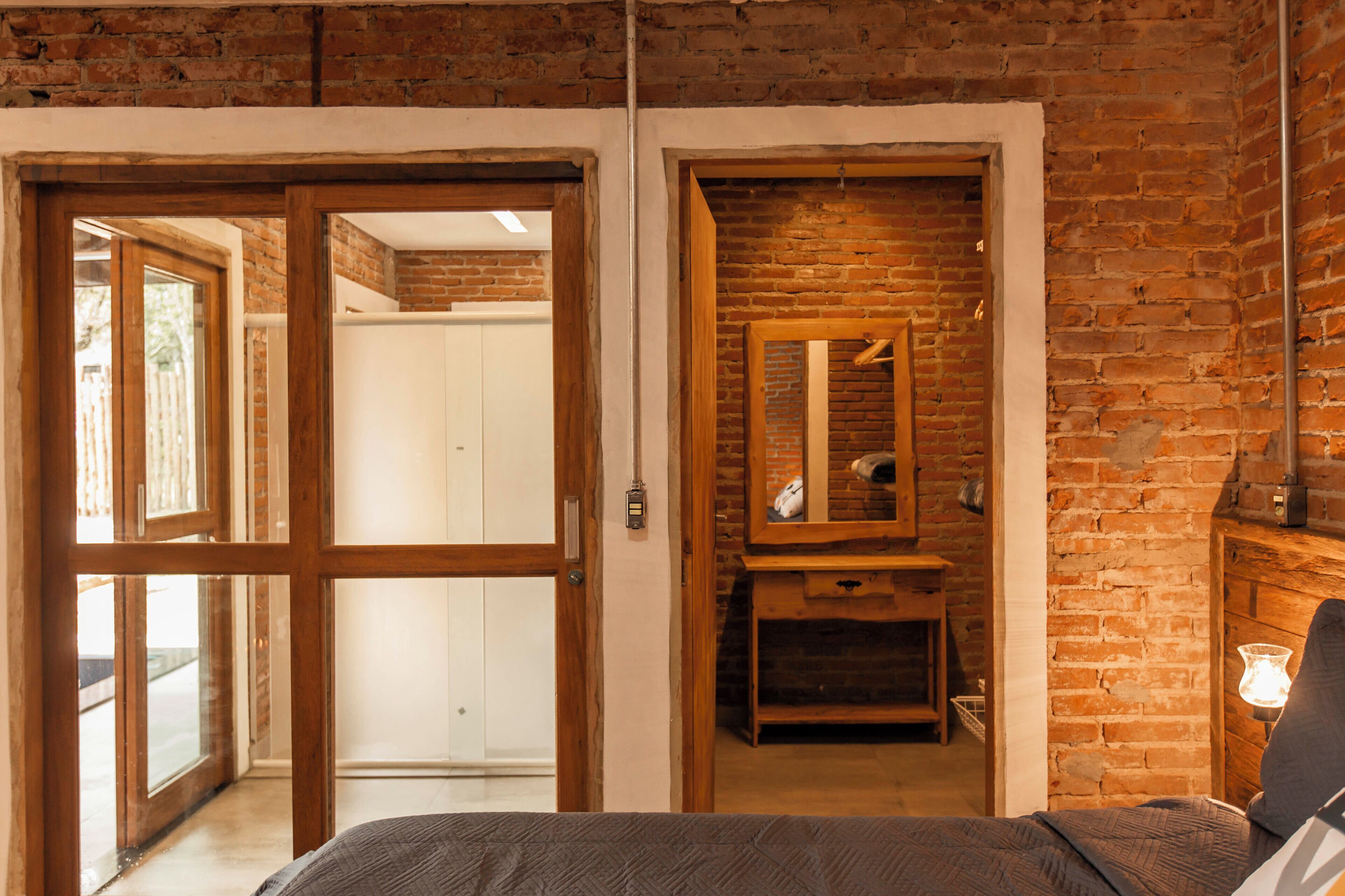 A room with a bed, a wooden dresser, a mirror, and a brick wall.