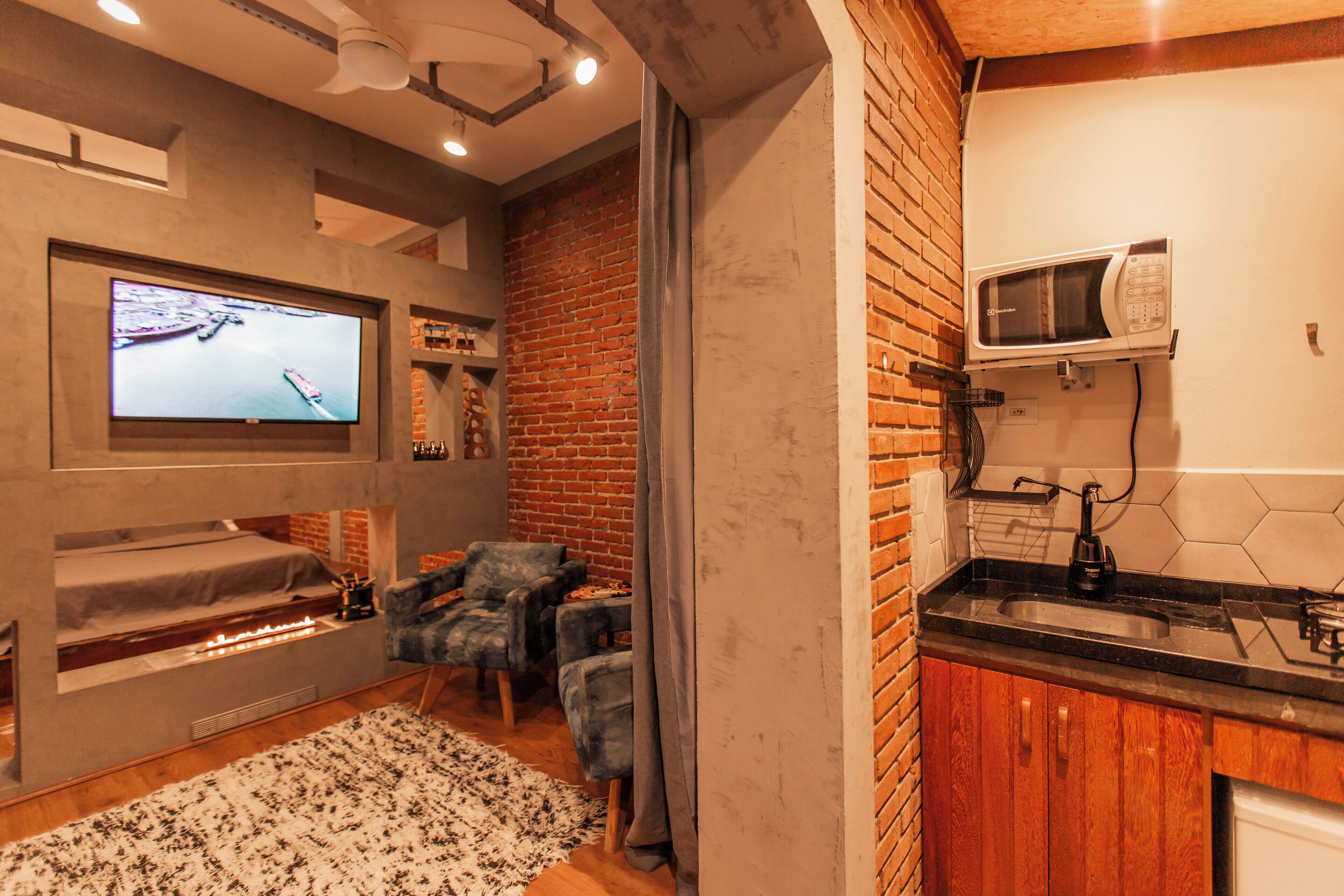 A modern living room with a fireplace, comfortable seating, a flat-screen TV, and a kitchen area with a microwave.