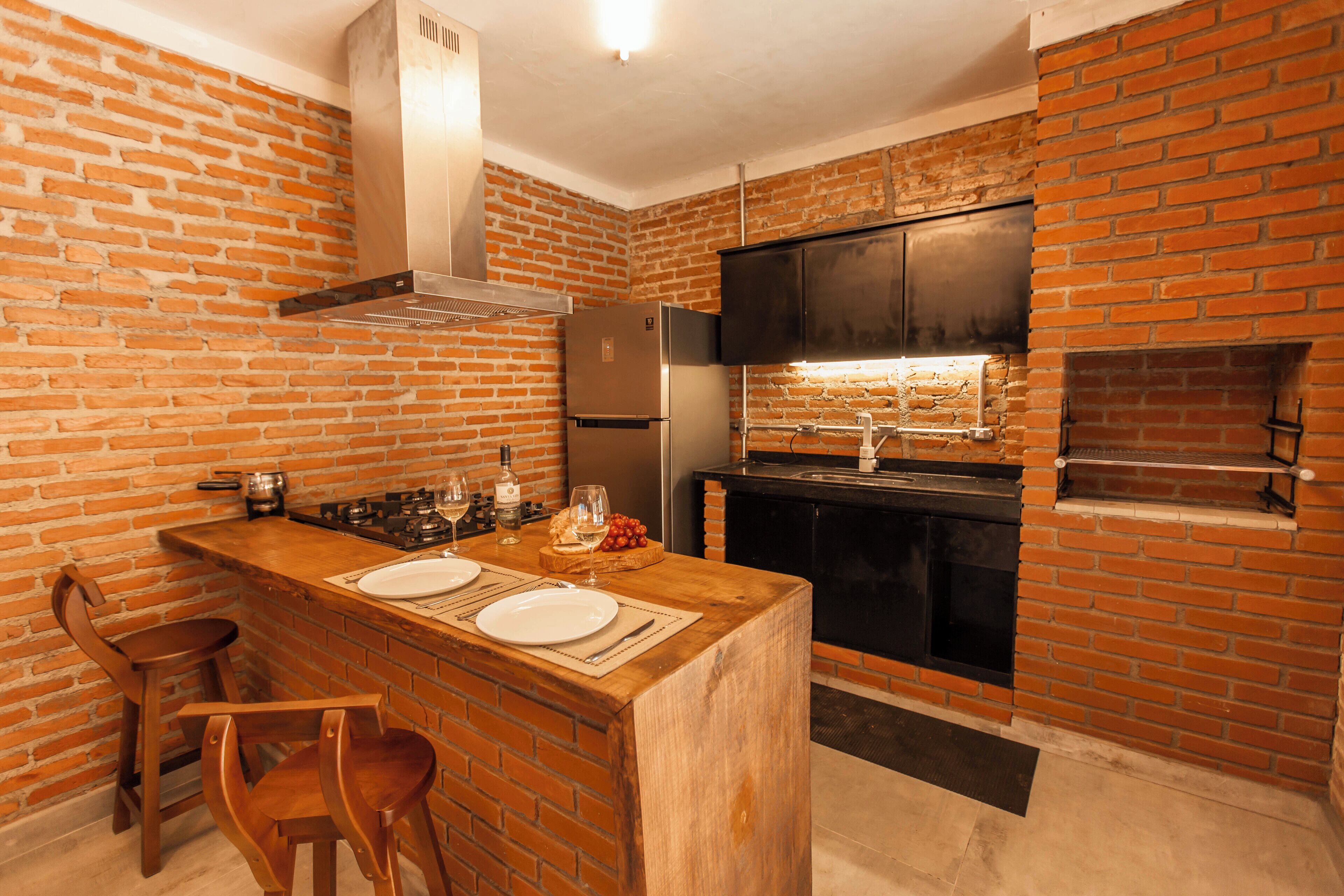 Una cocina con paredes de ladrillo, una barra de madera, dos taburetes de bar, un refrigerador, una estufa y un horno empotrado.