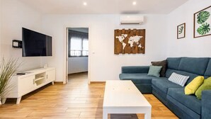 A modern living room with a flat-screen TV, a white coffee table, and a blue sofa with cushions.