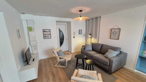A modern living room with a grey sofa, two armchairs, a small coffee table, and a ceiling light fixture. - Apartment n°1 : Sybèle (La Gaubretière)