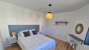 A bedroom with a bed, bedside tables, a desk, and a hanging light fixture. - Apartment n°1 : Sybèle (La Gaubretière)
