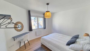 A bedroom with a bed, bedside table, chair, and a hanging light fixture. - Apartment n°1 : Sybèle (La Gaubretière)