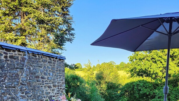 Ein Essbereich im Freien mit einer Steinmauer, einem Holztisch für vier Personen und einem großen Sonnenschirm.