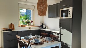 Eine moderne Küche mit dunklen Schränken, einer eingebauten Mikrowelle und einem Essbereich mit weißem Tisch und Stühlen.