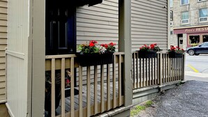 A building with a porch, a black door, and flower boxes with red flowers.