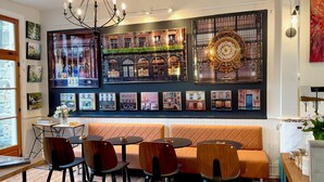 A restaurant interior with a long communal table, individual tables, cushioned seating, and a wall decorated with framed pictures.