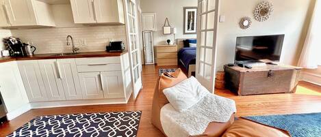 A compact living space with a kitchenette, a sofa, a television, and a patterned rug.
